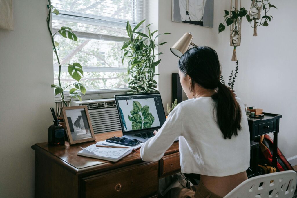 a woman sitting at a laptop surrounded by houseplants