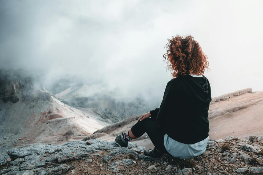 a woman sitting on top of a hill enjoying the view below